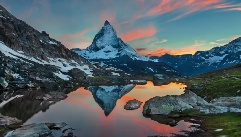 Zachód słońca nad jeziorem z odbiciem Matterhornu. Widok na wejście na Matterhorn, otoczone skalistymi zboczami i ośnieżonymi szczytami.