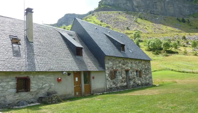 El refugio Vignemale, una construcción de piedra y pizarra, se alza en un prado verde bajo imponentes montañas rocosas.