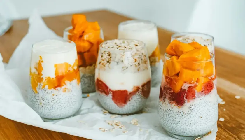 Sześć deserów z nasion chia, jogurtu i owoców (truskawki, mango) w szklankach.