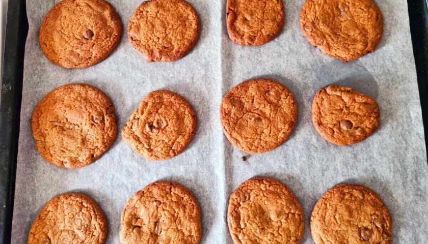 Nybakade chocolate chip cookies på bakplåtspapper. Perfekt för ett enkelt recept!