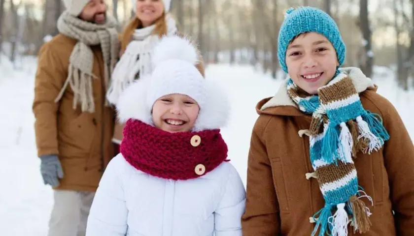 Familia sonriendo en un día de **invierno para niños**. Los niños al frente llevan abrigos y bufandas coloridas.