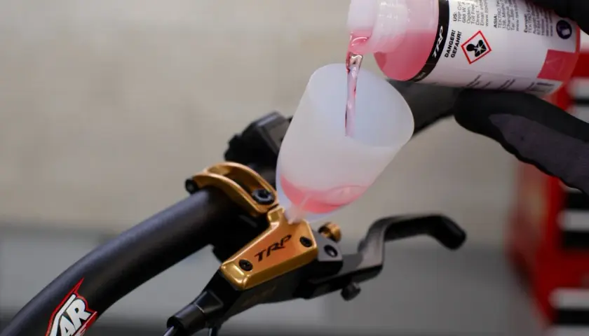 Adding brake fluid without bleeding is not recommended. This image shows pink fluid being poured into a funnel on a TRP brake lever.