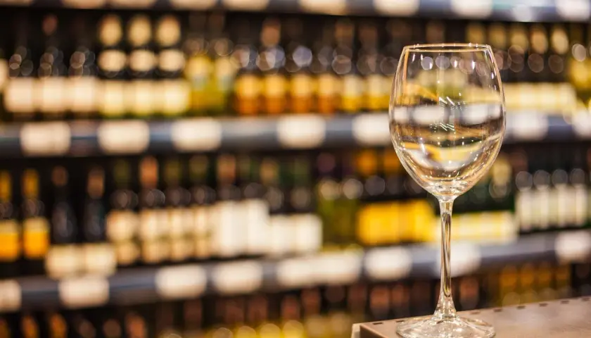 Verre à vin vide sur un comptoir, devant des étagères remplies de bouteilles. L'ambiance évoque une dégustation de vin à Paris.