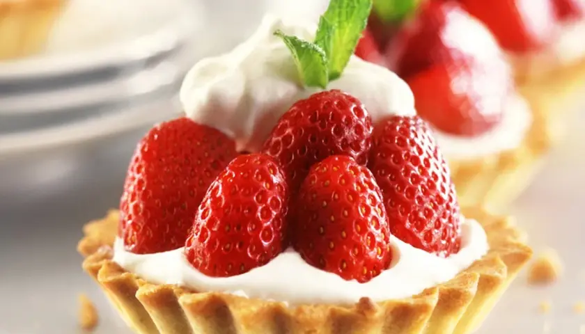 Deliziosi dolci con fragole fresche e panna montata, guarniti con una fogliolina di menta.
