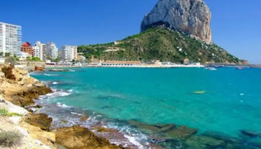 Vista del natural park of Penyal d'Ifac con aguas turquesas, rocas y edificios costeros.