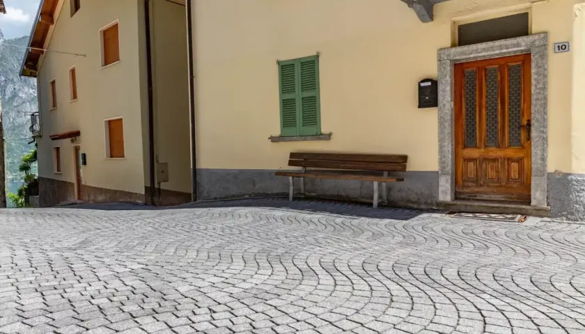 Pavimentazione in pietra per esterni carrabili, con case color pastello e un panchina.