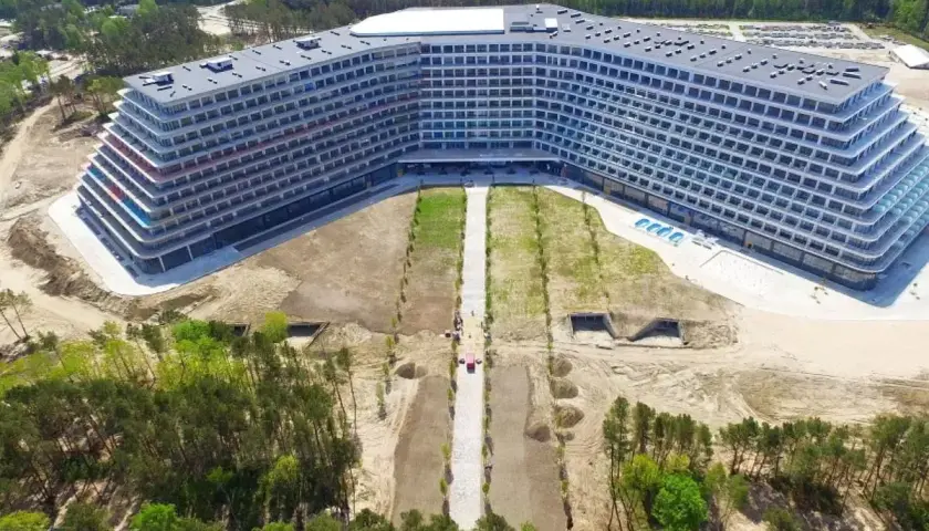 Nowoczesny hotel Gołębiewski w Pobierowie, z tarasami i basenem, otoczony lasem i placem budowy.