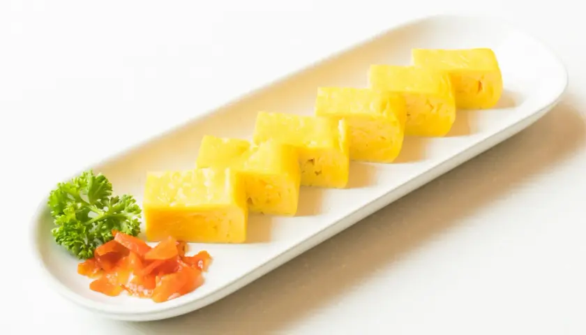 Japoński omlet tamagoyaki pokrojony w plastry, podany z natką pietruszki i marynowaną marchewką.
