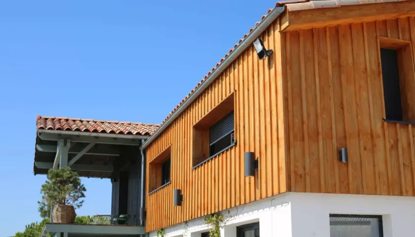 Bardage en bois naturel, un choix idéal pour l'extérieur. La maison moderne arbore des lames de bois clair sous un ciel bleu.