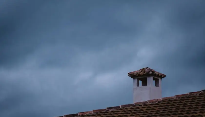 Komin na dachu, jakby pokryty folią w płynie, na tle burzowego nieba.