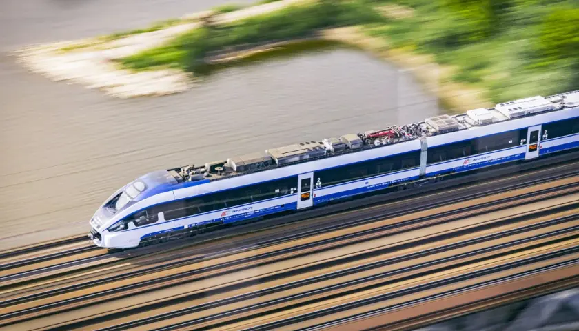 Pędzący pociąg Intercity w ruchu, z rozmytym tłem rzeki i zieleni.