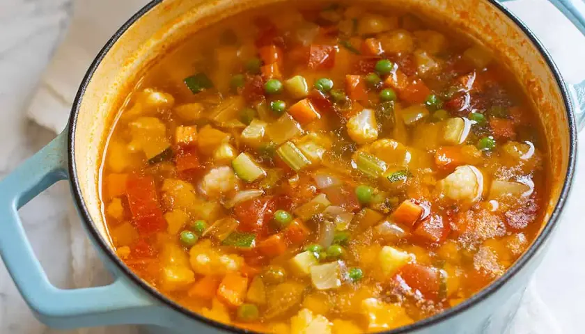 A close-up of a light blue pot filled with steaming minestrone soup, showing chunks of vegetables.