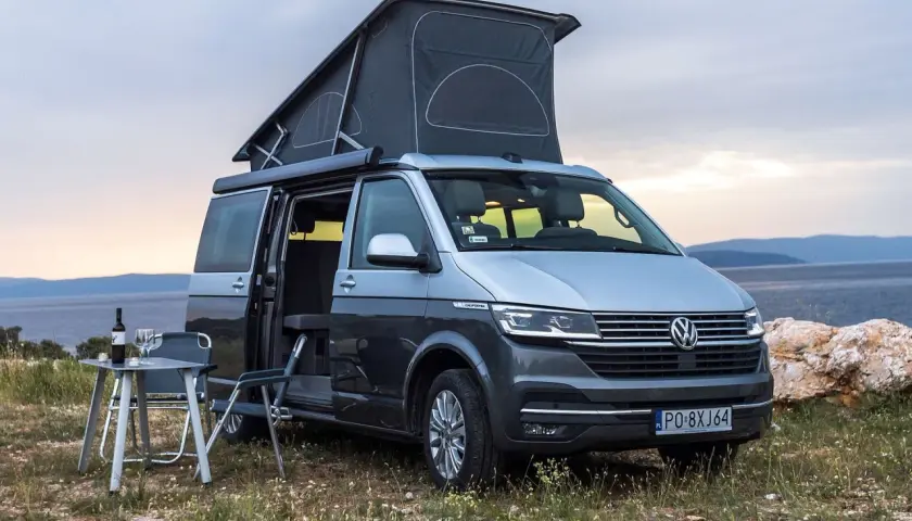 Szary kamper VW California z podniesionym dachem, idealny na wakacje. Poznaj jego wymiary i możliwości podróżnicze.