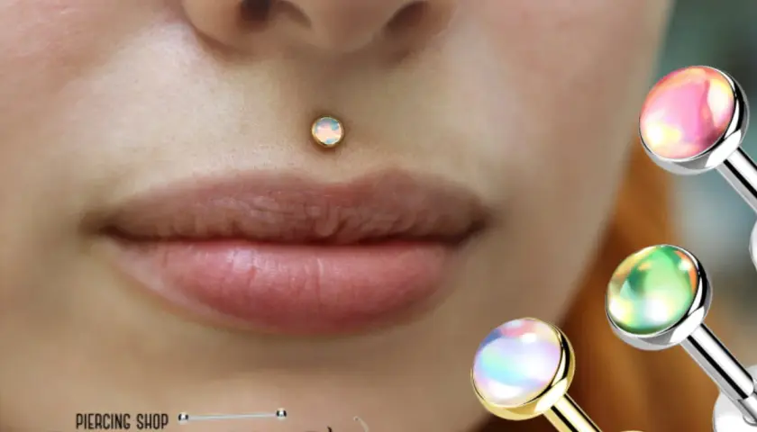 Delikatny labret kolczyk z opalem na ustach. W tle błyszczące ozdoby do piercingu.