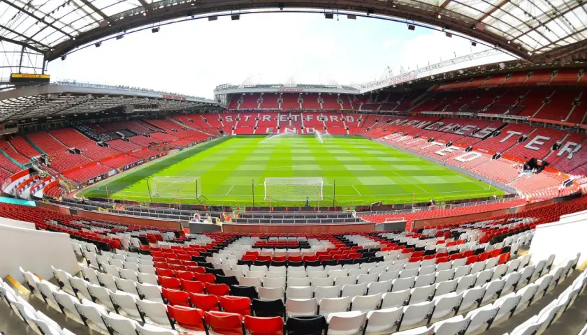 Widok na pusty stadion Old Trafford, z zieloną murawą i rzędami czerwonych, białych i czarnych siedzeń. Imponująca old trafford pojemność robi wrażenie.