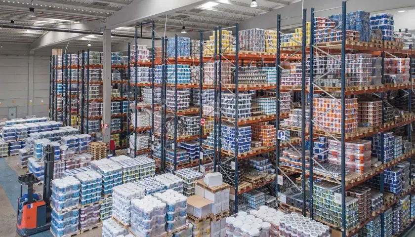 Großes Lager mit vielen Regalen voller Farbeimer und anderer Arbeitsmittel. Ein Gabelstapler steht bereit.