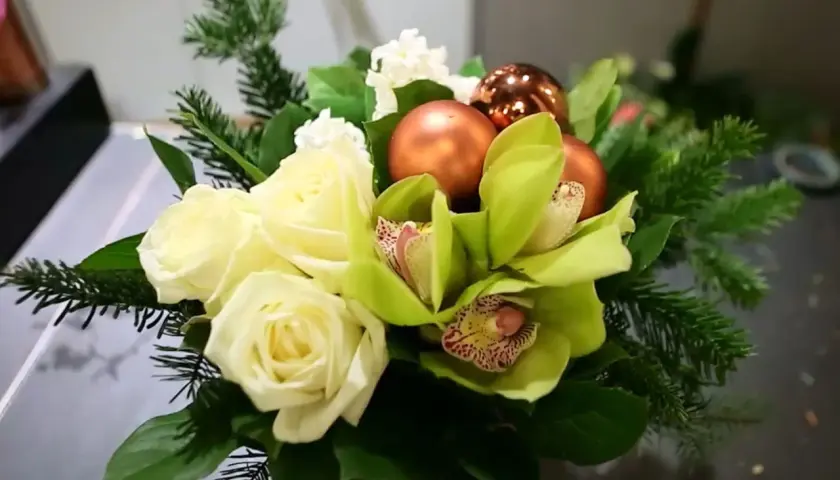 Un magnifique bouquet de noël à faire soi-même avec roses blanches, orchidées vertes, boules cuivrées et branches de sapin.