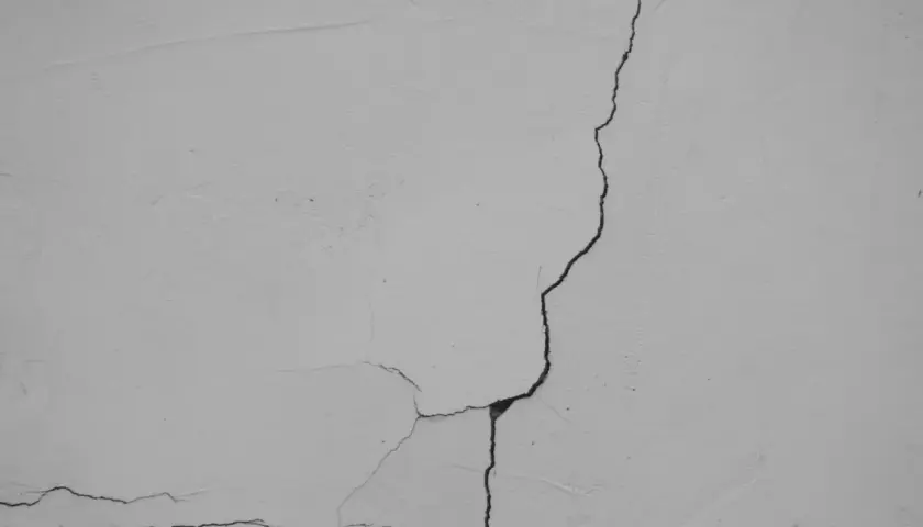 Widoczne pękanie ścian w narożnikach, tworzące sieć drobnych i większych szczelin na jasnej, tynkowanej powierzchni.