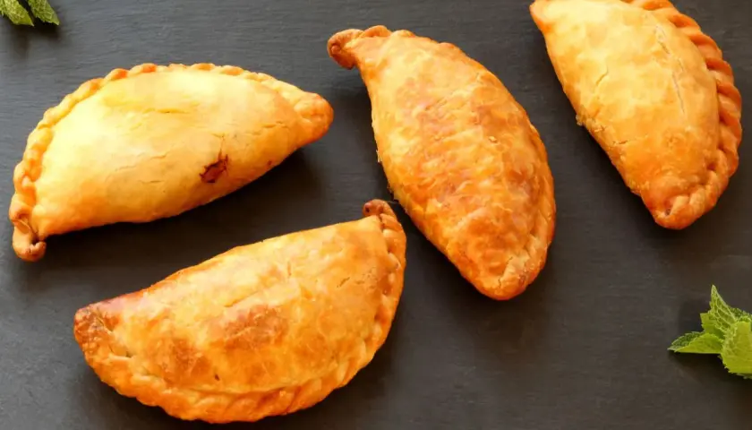 Cuatro empanadillas doradas y crujientes, recién hechas en freidora de aire, reposan sobre una pizarra oscura.