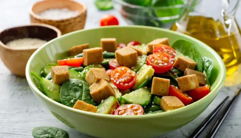 Pyszna sałatka z tofu, pomidorkami koktajlowymi, ogórkiem i szpinakiem, posypana sezamem. Idealna na lekki posiłek.