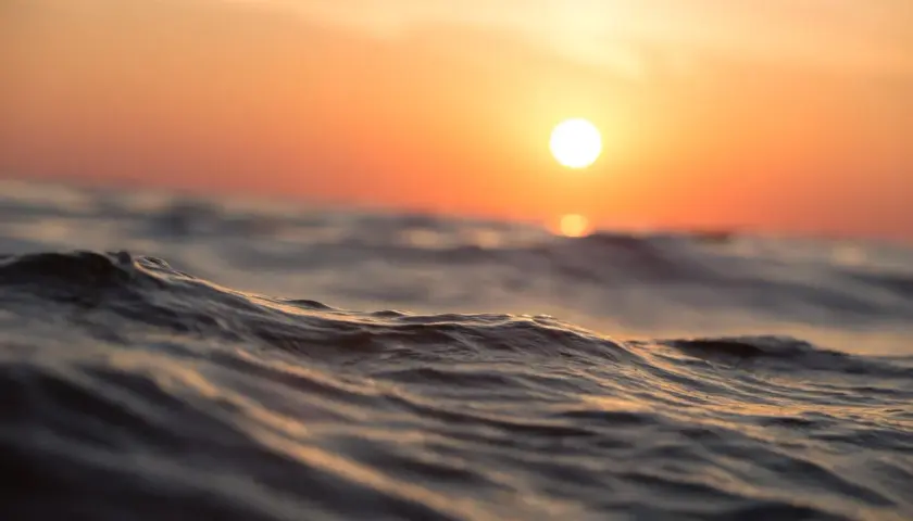 Olas suaves reflejan el atardecer anaranjado. Es como soñar con agua de mar, una paz que te envuelve.