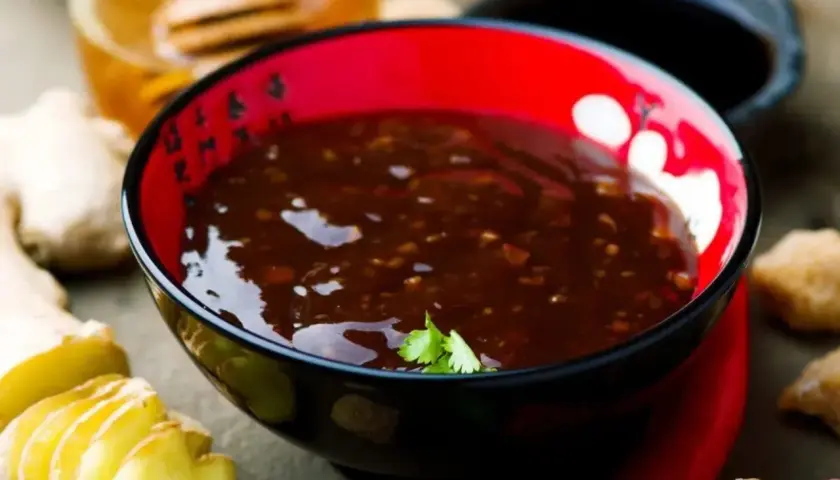 Schwarze Schüssel mit glänzender, dunkler Teriyaki-Sauce, umgeben von frischem Ingwer und Chili.