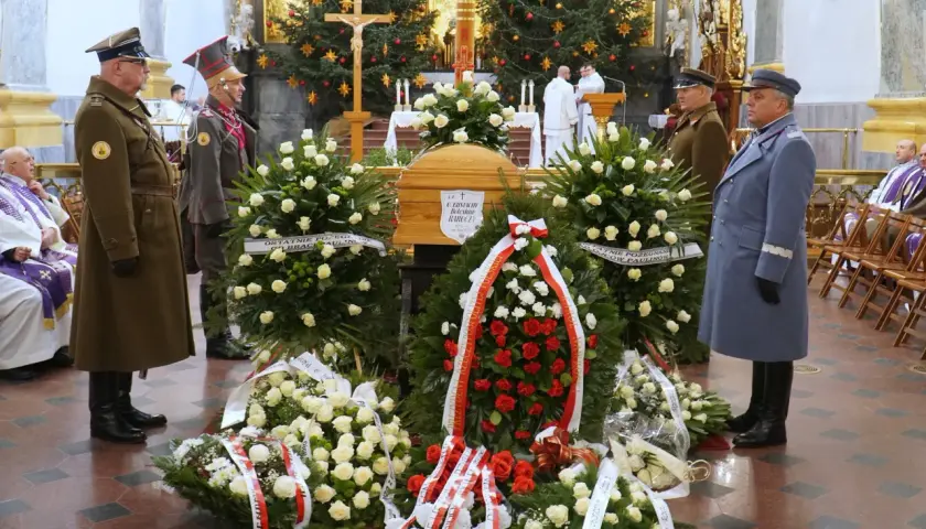 Trumna w otoczeniu wieńców, żołnierze w mundurach stoją na straży.