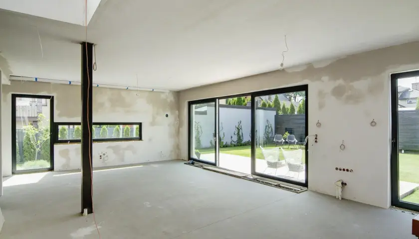 Wnętrze domu w budowie, przygotowane do tynkowania. Duże okna wychodzą na ogród. Szacowany koszt tynkowania domu 120m2.