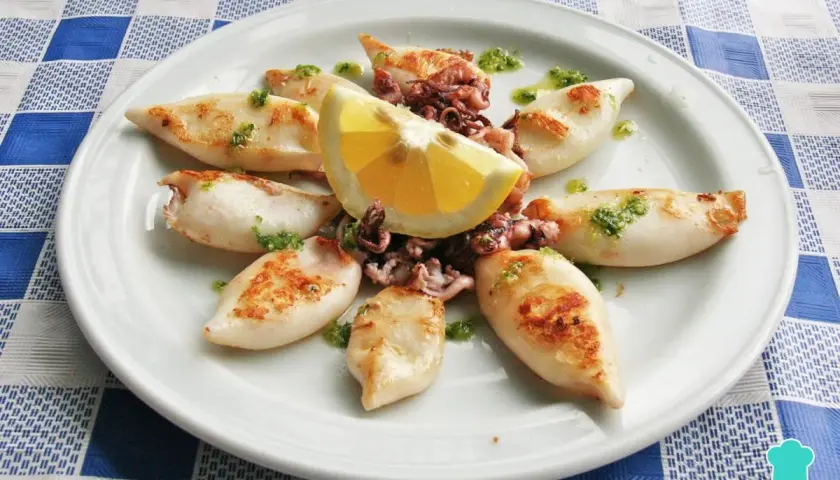 Chipirones a la plancha, tiernos y dorados, servidos con limón y un toque de perejil picado. Un plato sencillo y delicioso.