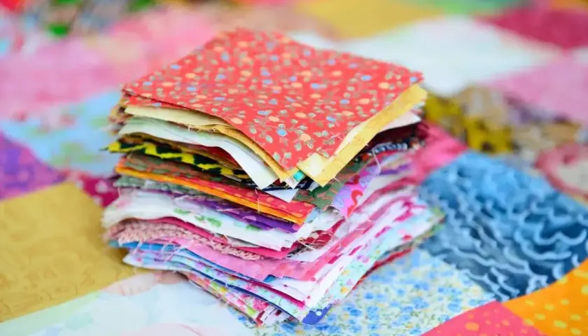 Stos kolorowych kwadratów materiałów, gotowych do stworzenia patchworku. To właśnie patchwork – sztuka łączenia skrawków tkanin w piękne wzory.