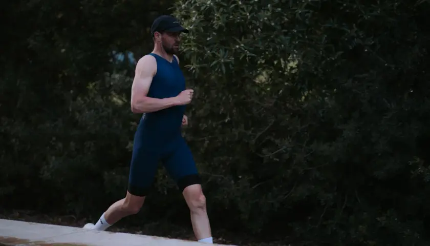 Mann in dunkelblauem Triathlonanzug läuft vor dunklem Grün.