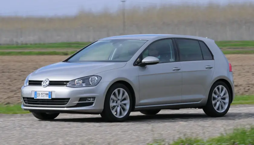 Volkswagen Golf 1.6 TDI argento in movimento su strada sterrata, con campi coltivati sullo sfondo.
