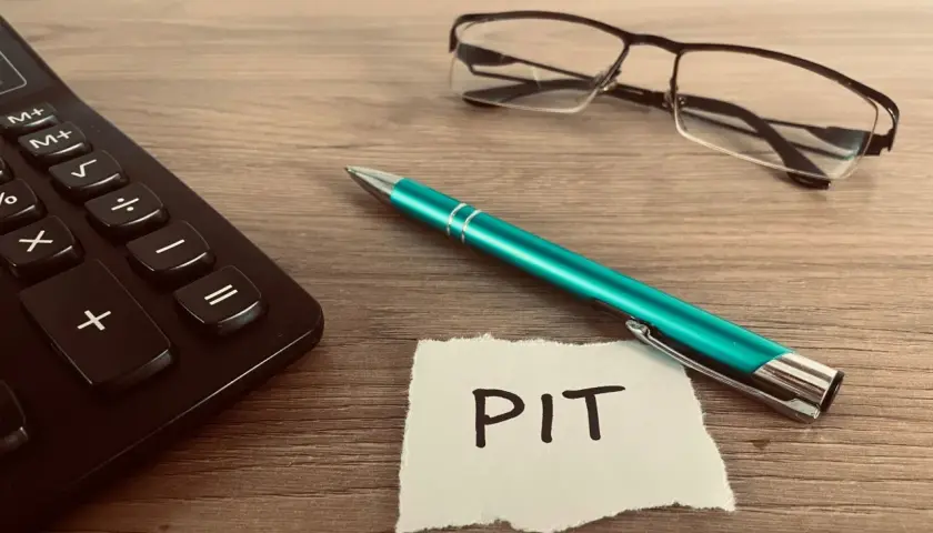 Kalkulator, zielony długopis i okulary leżą obok kartki z napisem PIT. Czas rozliczyć PIT 36L.
