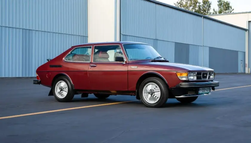 En röd Saab 99 Turbo står parkerad framför en blå hangar.