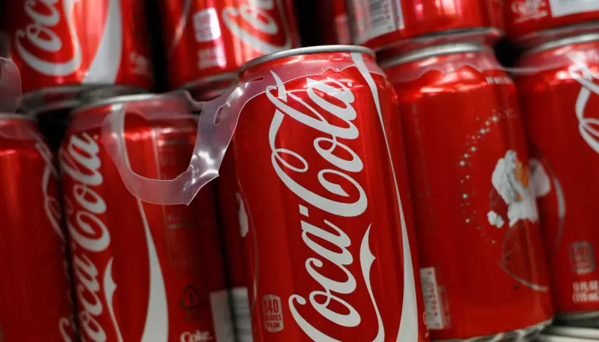 Puszki Coca-Coli ułożone na półce, jedna z nich z widoczną etykietą kaloryczną.