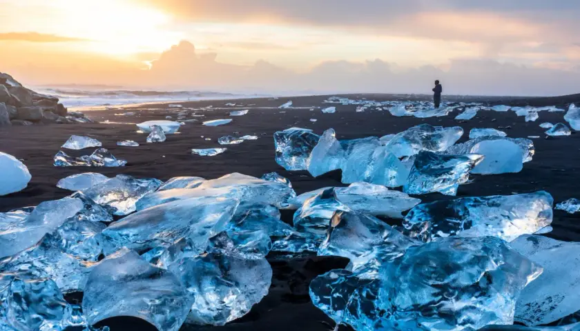 Fragmentos de hielo brillan en la arena negra del Diamond Beach de Islandia, bajo un cielo crepuscular.