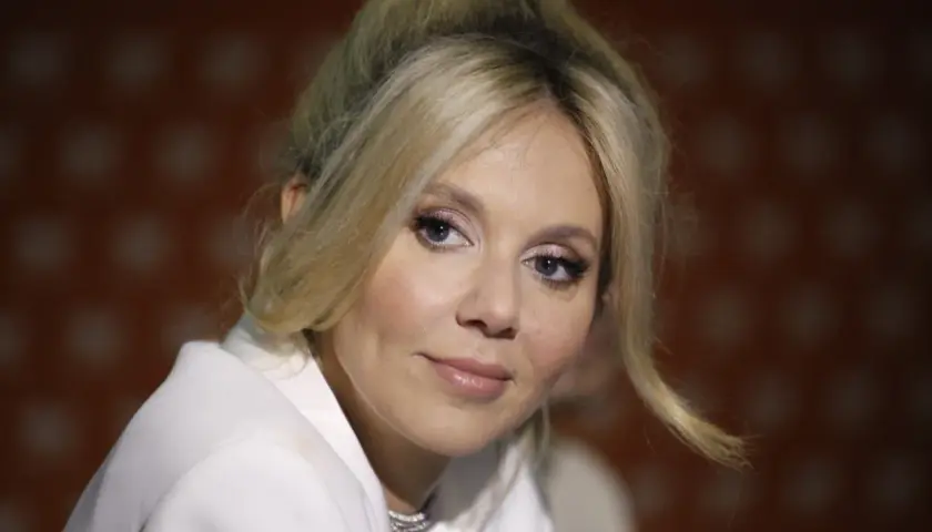Kasia Moś, której wiek dodaje jej uroku, w białej marynarce z błyszczącym naszyjnikiem.