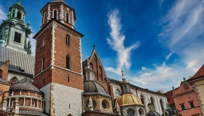 Kraków: Wawel z ceglaną wieżą, złotą kopułą i zielonym dachem pod błękitnym niebem.