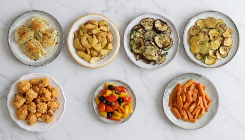Sette piatti di verdure in friggitrice ad aria: finocchi, patate, melanzane, zucchine, cavolfiore, peperoni e carote.