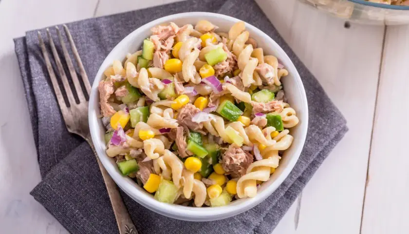 Ein köstlicher nudelsalat mit thunfisch, garniert mit Mais, Gurken und roten Zwiebeln, bereit zum Genießen.