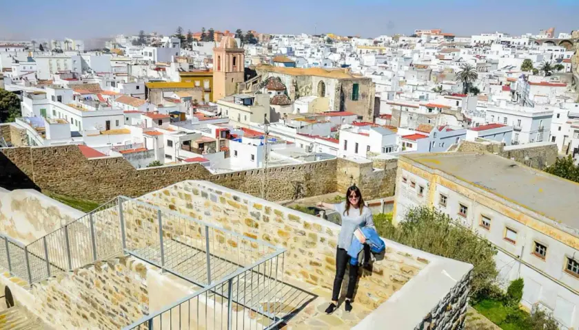 Una mujer sonríe en un balcón de piedra con vistas a un pueblo blanco. ¡Descubre todo **que ver en Tarifa**!