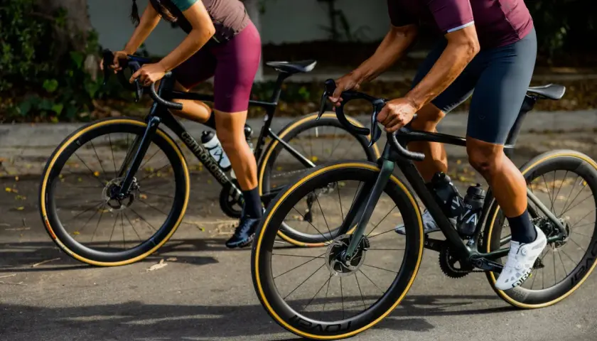 Two cyclists on road bikes, one with a blue book in their jersey pocket, showcase the value of a high-performance bike.