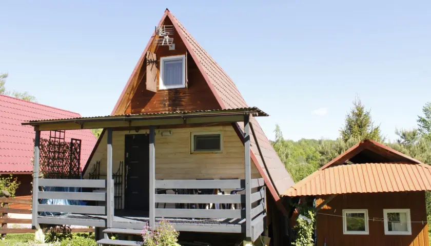 Drewniany olchowiec nad Soliną, z czerwonym dachem i werandą, otoczony zielenią.