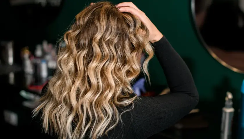 Blond włosy z falami, ułożone z pomocą aktywatora skrętu. W tle kosmetyki fryzjerskie.