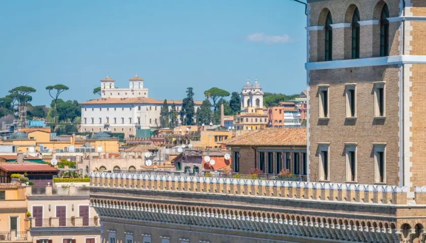 Vue panoramique de Rome, avec la Villa Médicis et ses jardins en arrière-plan, sous un ciel bleu clair.
