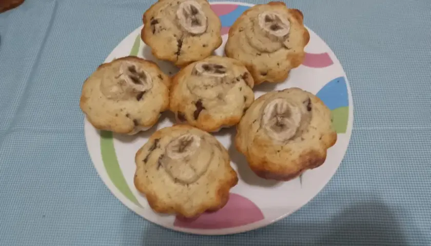 Sei muffin banana e cioccolato, guarniti con una fetta di banana, su un piatto colorato.