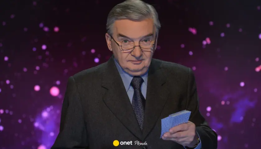 Tadeusz Sznuk w garniturze, z okularami na nosie, trzyma w dłoni małe niebieskie karty. Może to być nawiązanie do jego żony, która kiedyś grała w karty.