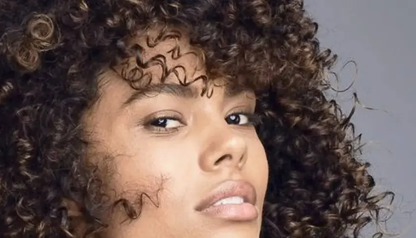 Mujer con cabello rizado y oscuro, mostrando cómo nutrir el pelo para un brillo saludable.
