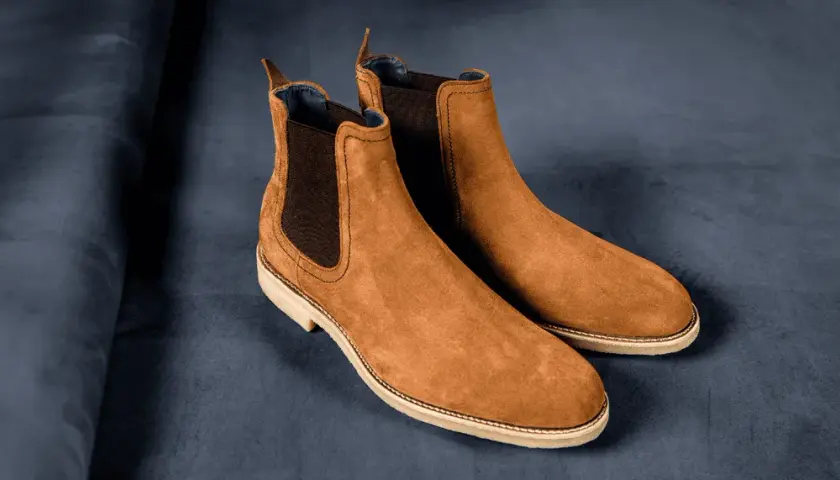 Paire de bottines Chelsea en daim marron, sur fond bleu nuit. La matière daim offre une texture douce et luxueuse.