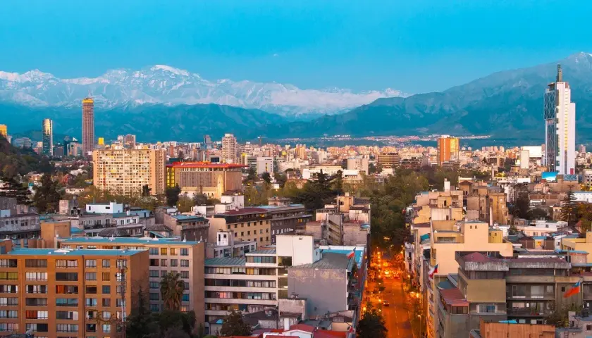 Widok na Santiago, stolicę Chile, z górami w tle. Miasto tętni życiem, a światła uliczne rozświetlają wieczór.